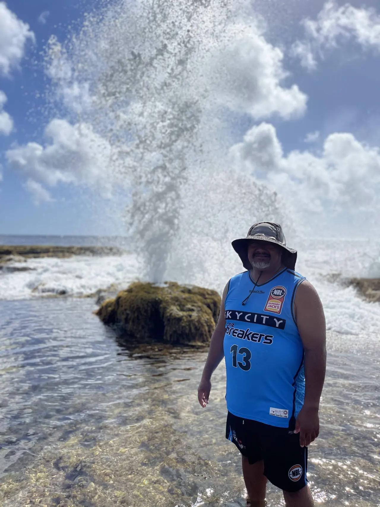 A visitor standing beside the Mapuʻa ʻa Vaea Blowholes as sea spray rises behind